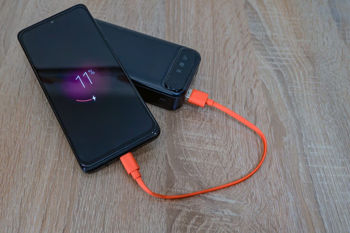 A phone on charge beside a power bank, linked by an orange cable during a battery drain and recovery run