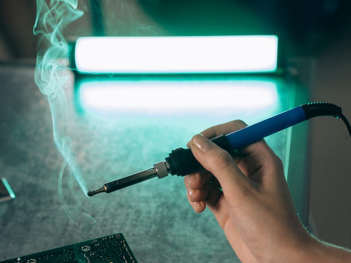 A soldering iron in use over a circuit board at the repair bay